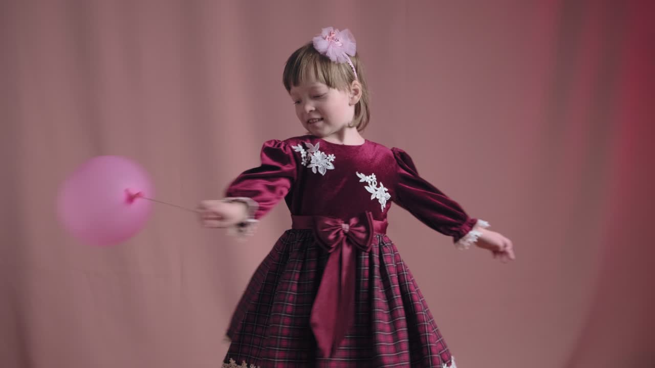 Cute little girl in vintage burgundy dress is playing with pink inflatable ball