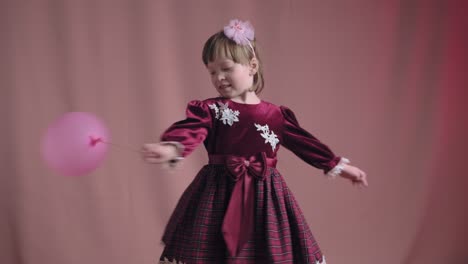 cute little girl in vintage burgundy dress is playing with pink inflatable ball