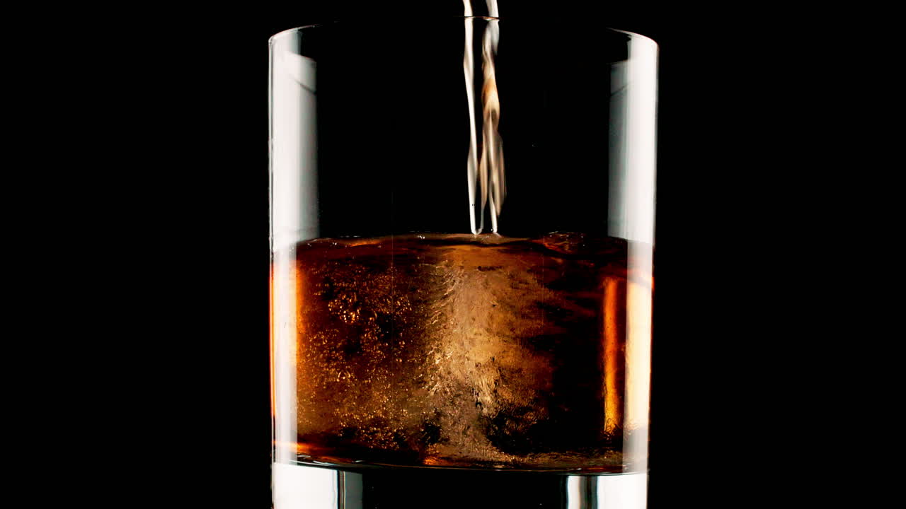 A refreshing drink being poured into a glass with ice