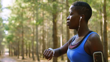 female jogger using smartwatch in the forest 4k