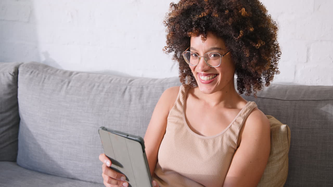 Woman using tablet on gray sofa, concentrating on screen at home, copy space