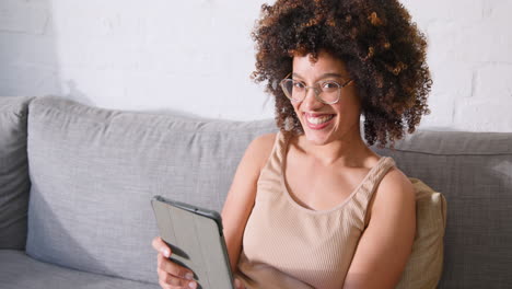 woman using tablet on gray sofa, concentrating on screen at home, copy space