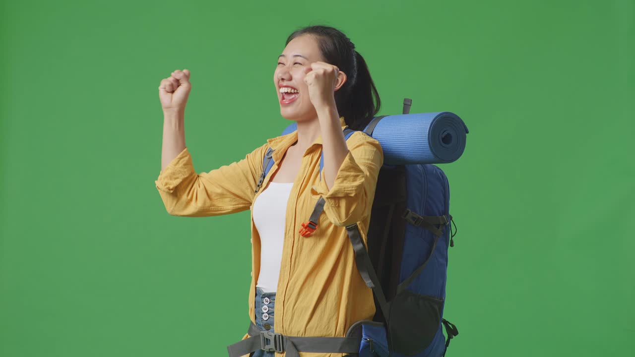 vista lateral de una excursionista asiática con mochila de montañismo gritando meta celebrando el éxito mientras está de pie en el fondo de la pantalla verde en el estudio