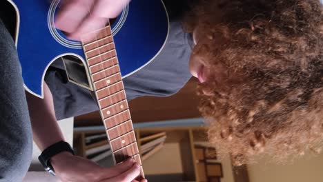 a young curly red-haired guy is learning to play the guitar. a talented guitarist plays a calm melody. hobby