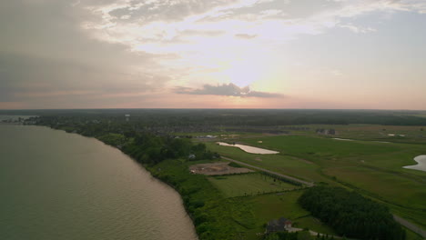 Amplia-Vista-De-Drones-De-La-Puesta-De-Sol,-Cabañas,-Campos-Y-Suburbios-Cerca-De-La-Orilla-Del-Lago