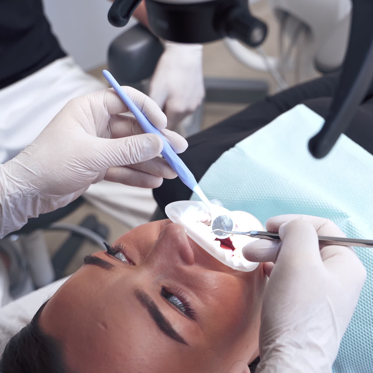 Young woman laying in the dental chair. Dentist treating patient's teeth in the dental office. Stomatologist examines teeth through the microscope.