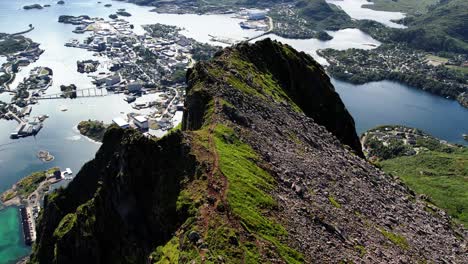 Aerial-shot-of-a-steep-mountain-peak-on-a-sunny-day-with-the-city-of-Svolvaer-behind-it