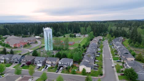 Orbiting-drone-shot-around-a-suburban-water-tower-with-an-elementary-school-in-the-background
