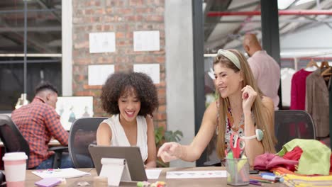 dos diseñadoras felices y diversas sentadas y discutiendo diseños en un estudio de moda, en cámara lenta