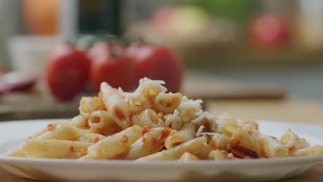 grated cheese falling over hot penne pasta with tomato sauce on plate
