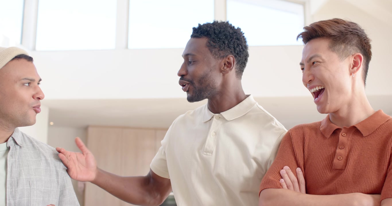 Diverse male friends leaning at open-plan kitchen loft while left man showing tablet and joking