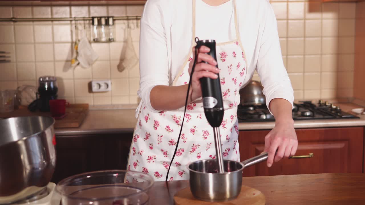 mujer preparando una salsa de frutas en una cocina usando una licuadora y un mezclador de soporte
