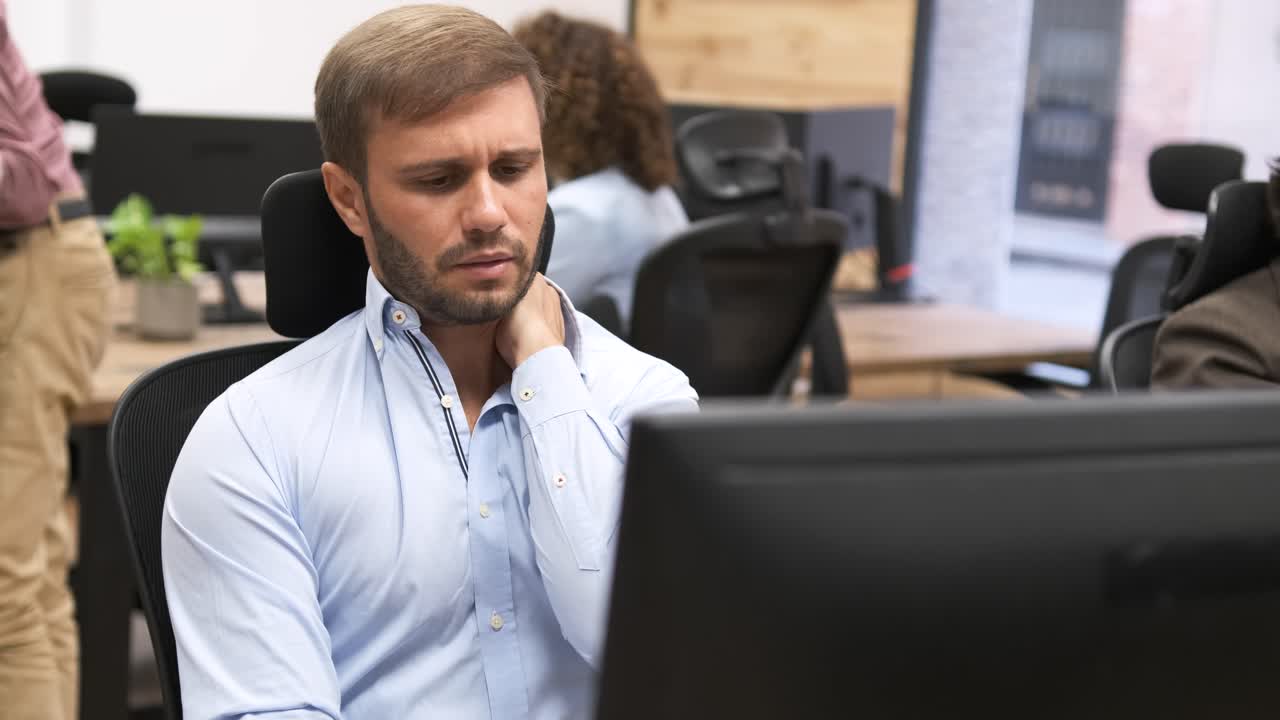 Müder Geschäftsmann massiert seinen Nacken, während er im Büro am Computer arbeitet