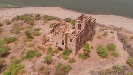 Toma-Aérea-De-Paralaje-De-Un-Edificio-Abandonado-En-Una-Pequeña-Isla-En-El-Embalse-De-Chotiari-En-Sindh,-Pakistán