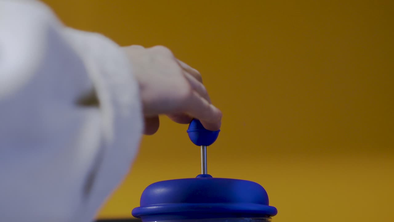 밝은 파란색 플런저를 아래로 누르는 손으로 선명한 노란색 배경