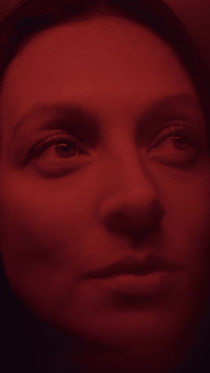 Ritratto di donna che guarda in alto sotto una luce neon rossa con transizione sfocata