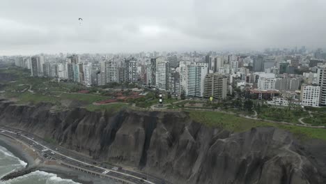 Paragliders-drift-over-clifftop-lighthouse-in-dense-overcast-Peru-city