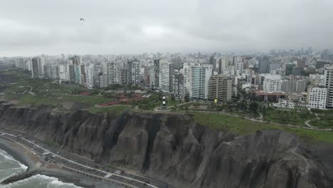 paragliders drift over clifftop lighthouse in dense overcast peru city