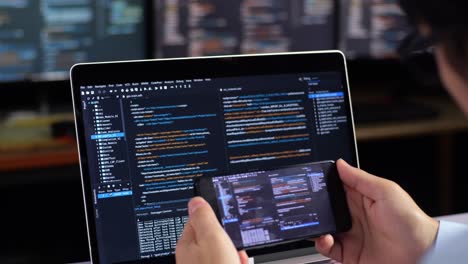 programmer working on code on laptop and smartphone