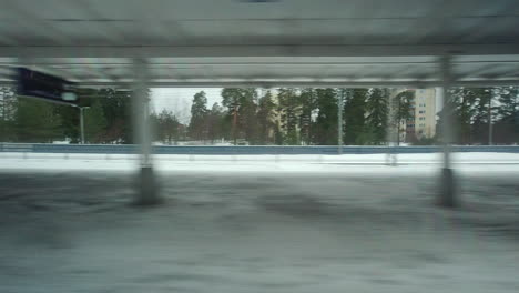 From-snowy-winter-commuter-train-window,-station-platform-passes