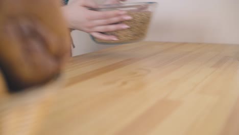 woman takes glass bowl full of grains from wooden table