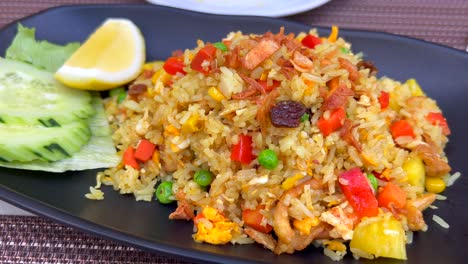 Spicy-fried-rice-with-chicken,-vegetables,-crispy-onion-and-cucumbers-at-a-Thai-restaurant,-tasty-traditional-asian-food,-4K-shot