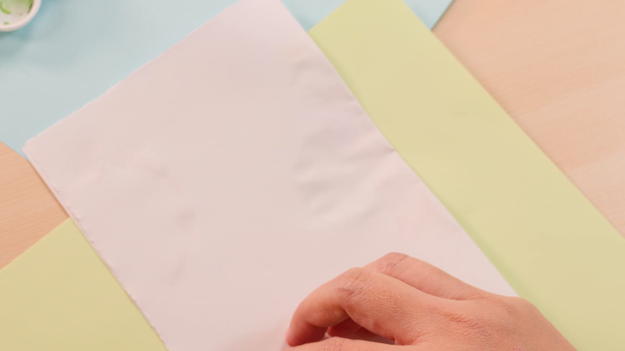 Hands fold paper to reveal colorful symmetrical paint blot artwork in bright classroom lighting