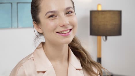 portrait of a cute happy woman in pink pajamas sitting in bed and posing to the camera