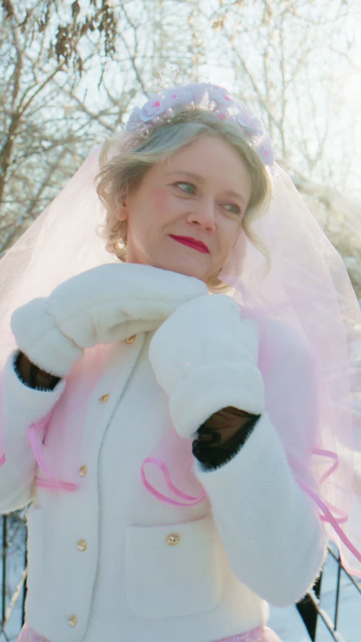 Femme heureuse avec un voile rose et des moufles blanches posant dans un hiver enneigé