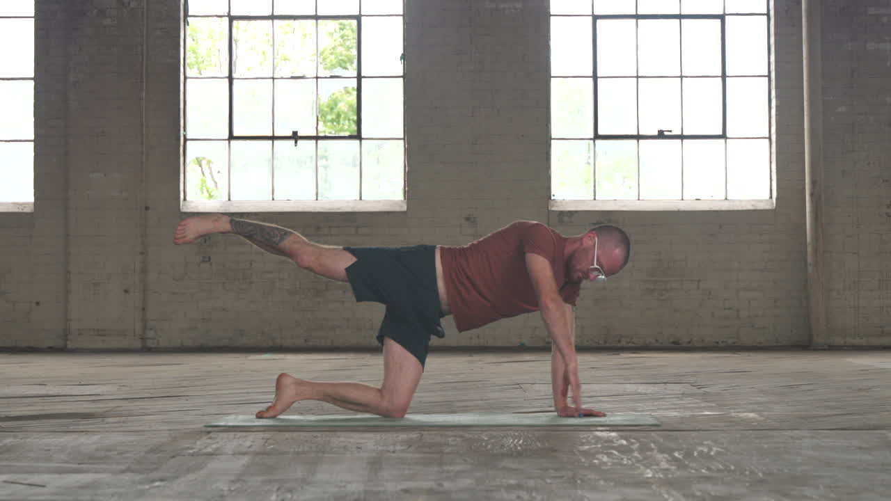 Man in an industrial warehouse practicing yoga, the pose of an assisted plank.