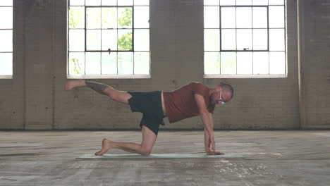 man in an industrial warehouse practicing yoga, the pose of an assisted plank.