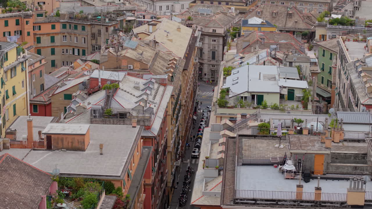 Drone moves laterally above the rooftops of the historical center of Genoa, Italy, showing colorful old buildings and a street with moving vehicles and a bus
