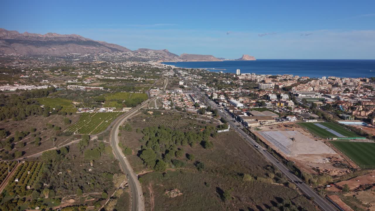 Albir, Costa Blanca Spagna. Rivelazione panoramica dall'alto e in lontananza di Albir con la campagna spagnola e gli aranceti in primo piano, viste distanti del mare, Benidorm e le montagne sotto un sole splendente con cielo blu