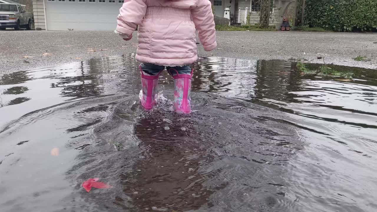 Walking slowly behind a little girl walking through a puddle wearing pink rubber boots