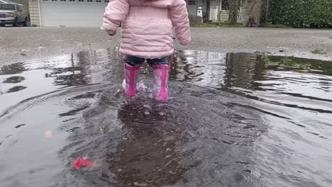 walking slowly behind a little girl walking through a puddle wearing pink rubber boots