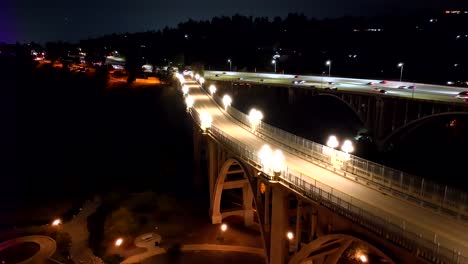 Aerial-view-rising-above-illuminated-Colorado-street-bridge,-Pasadena-California-during-blue-hour-with-highway-traffic