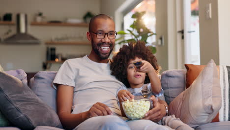 father and son watching tv and eating popcorn on the couch