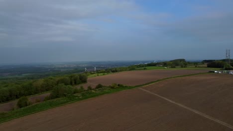 Aerial-view-overlooking-British-farmland-countryside-to-reveal-hilltop-telecommunications-towers