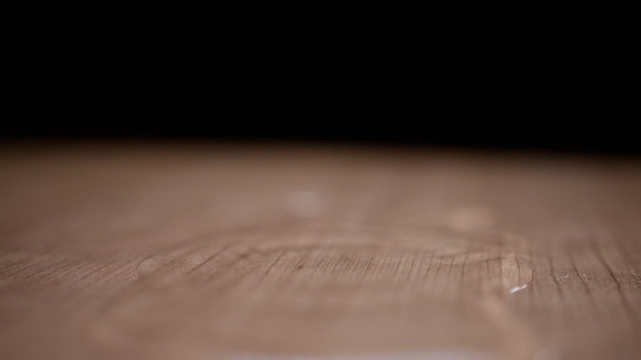 Super slow motion water drops falling on a wooden surface, creating ripples