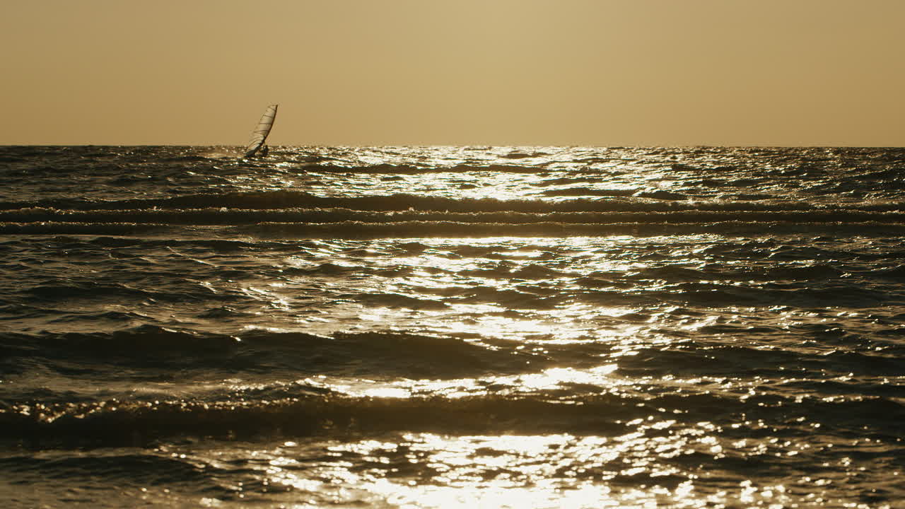 windsurfista solitario flotando en una tabla con una vela al atardecer