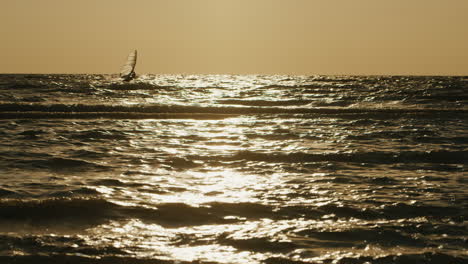 Einsamer-Windsurfer,-Der-Bei-Sonnenuntergang-Auf-Einem-Brett-Mit-Einem-Segel-Schwimmt