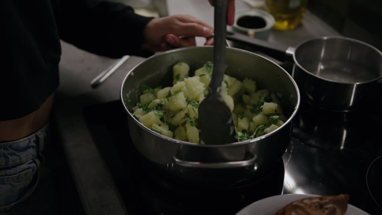 tomas de primer plano de manos mezclando patatas en una olla en la estufa usando un girador, mujer cocinando la cena en la cocina, patatas trituradas con perejil, acompañamiento europeo, comida vegetariana, dieta vegana, olla