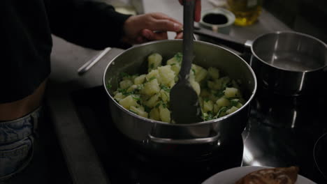 Primeros-Planos-De-Manos-Mezclando-Patatas-En-Una-Olla-En-La-Estufa-Usando-Un-Tornero,-Mujer-Cocinando-La-Cena-En-La-Cocina,-Patatas-Trituradas-Con-Perejil,-Guarnición-Europea,-Comida-Vegetariana,-Dieta-Vegana,-Olla