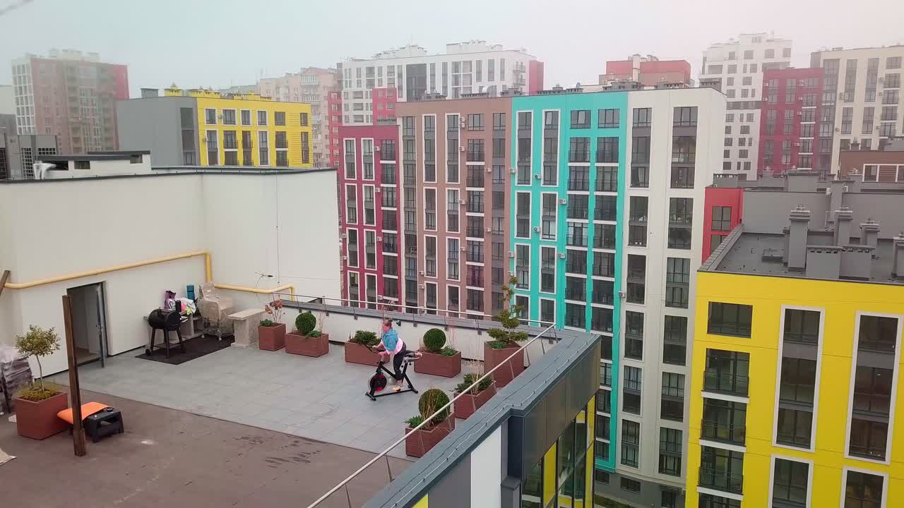 Athletic woman riding on spinning stationary bike training routine on house rooftop weight loss