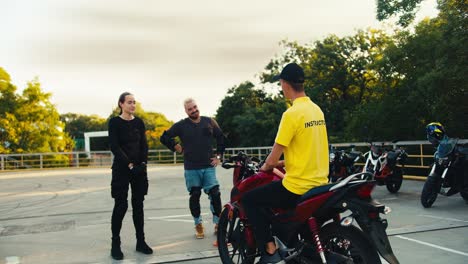 Happy-students-in-moto-school-chatting-with-moped-driving-instructor.-A-man-in-a-yellow-T-shirt-communicates-with-a-man-with-a-beard-and-a-girl