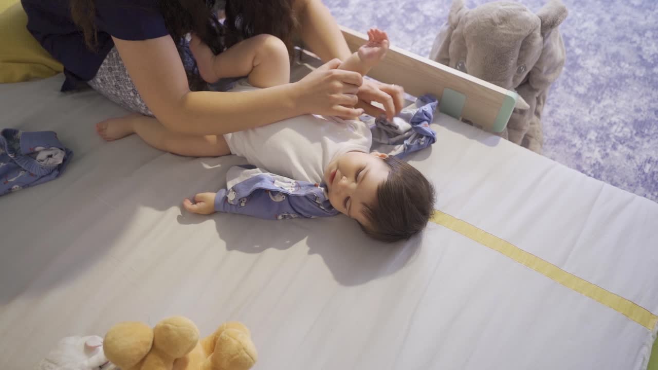 The mother taking off the baby's clothes in her bed.