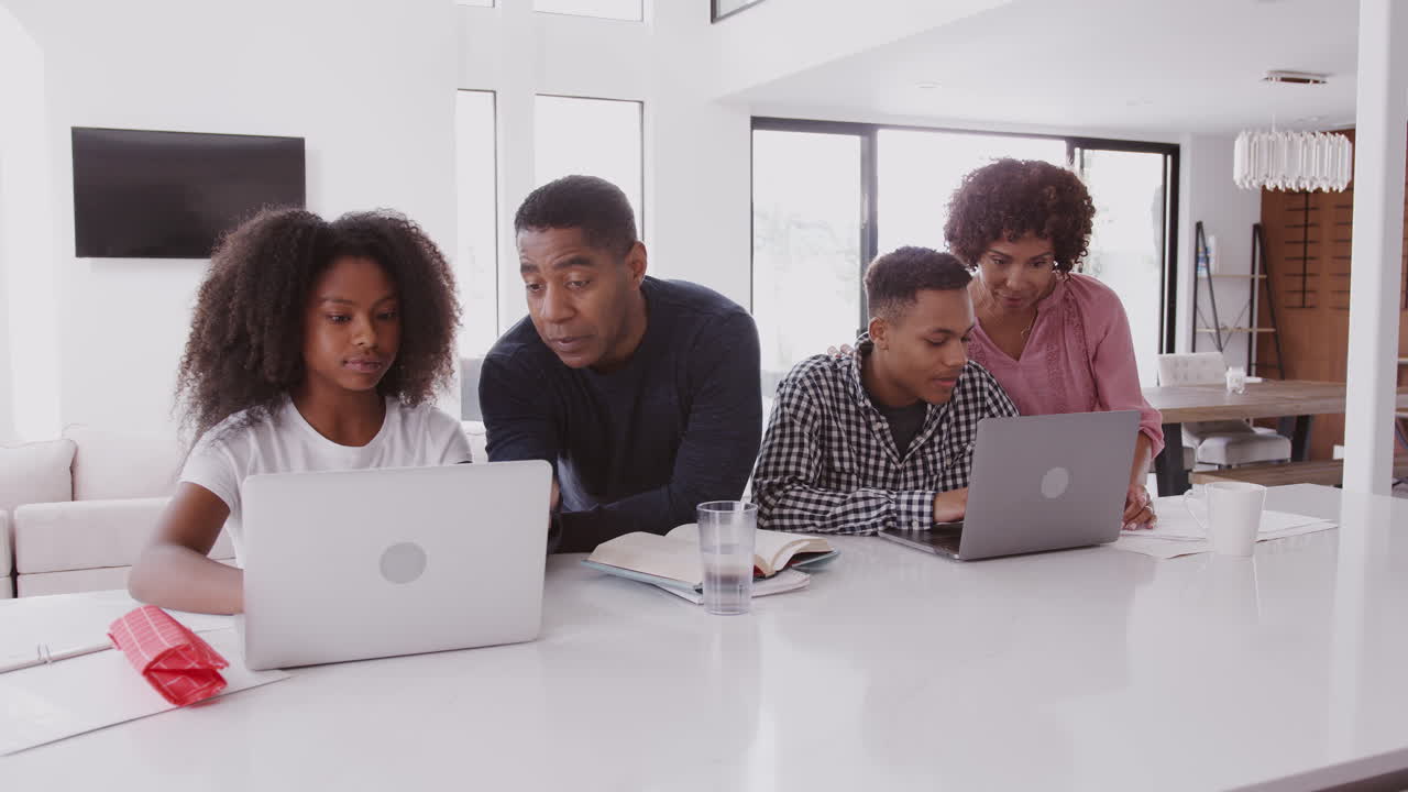 Middle aged black parents helping their teenage kids, doing their homework using laptops
