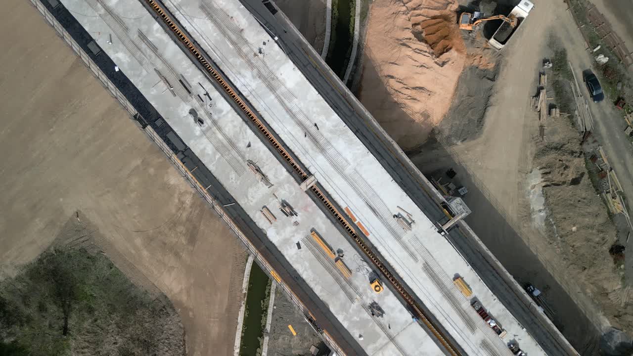 Top-down view of a bridge under construction showing workers, vehicles, and surrounding site details