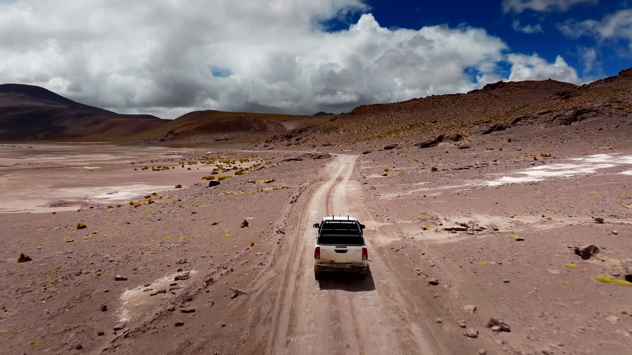 Drone tracking shot of utility vehicle driving on dirt road in Siloli desert