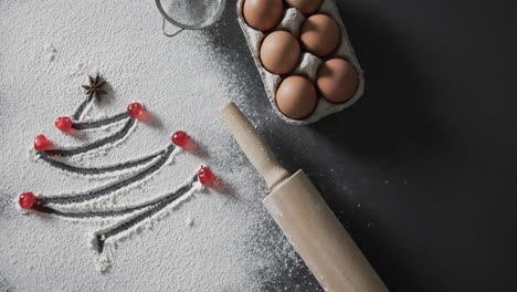 video of christmas tree drawn in flour, eggs, roler and copy space on black background